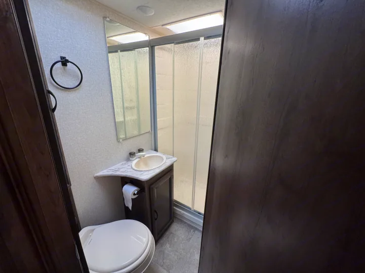 Compact RV rental bathroom featuring a white toilet, small sink, and glass-doored shower. Efficient design.. Forest River Coachmen Freelander 2019