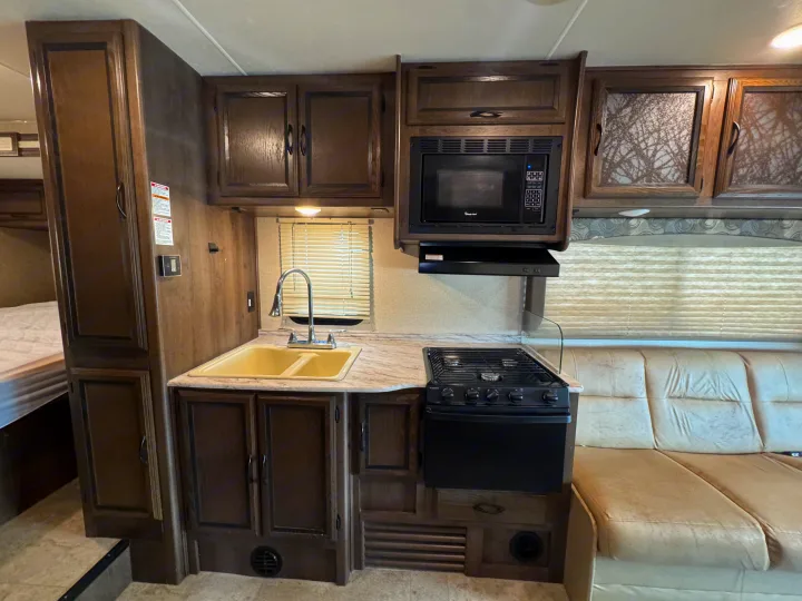 This rv rental showcases a compact kitchen with a sink, stove, microwave, and ample cabinets, next to a comfortable living area.. Forest River Coachmen Freelander 2019