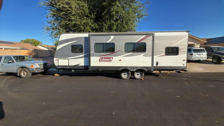 This Coleman RV rental, a travel trailer, is parked on an asphalt surface in a sunny residential setting.. Dutchmen Coleman Lantern 2018