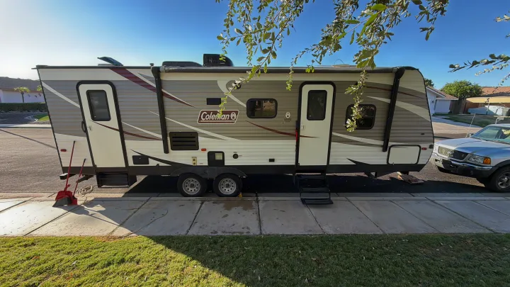 A large Coleman travel trailer, ready for rv rental, parked on a sunny residential street with a pickup truck and green lawn.. Dutchmen Coleman Lantern 2018