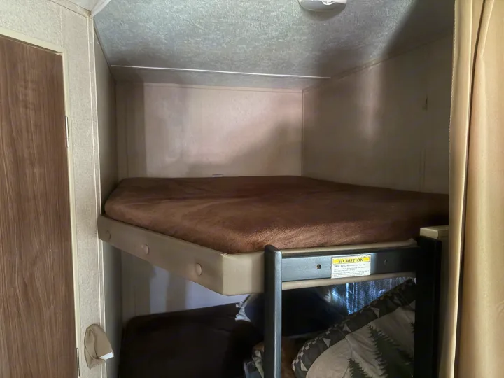 Cozy RV rental bunk beds with a brown fuzzy mattress on the top bunk, featuring a 300 lb weight limit.. Dutchmen Coleman Lantern 2018