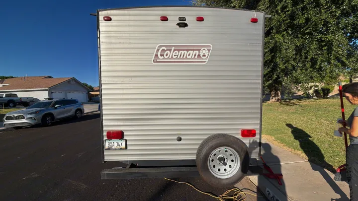 A Coleman RV rental's rear, showing an Arizona license plate, spare tire, and a person cleaning nearby.. Dutchmen Coleman Lantern 2018