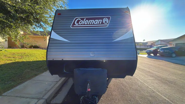 Sunny front view of a gray Coleman travel trailer RV rental, parked on a residential street. Hitch visible.. Dutchmen Coleman Lantern 2018