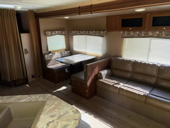 This rv rental showcases a comfortable interior with a dining booth, sofa, kitchen counter, and sunlit windows.. Dutchmen Coleman Lantern 2018