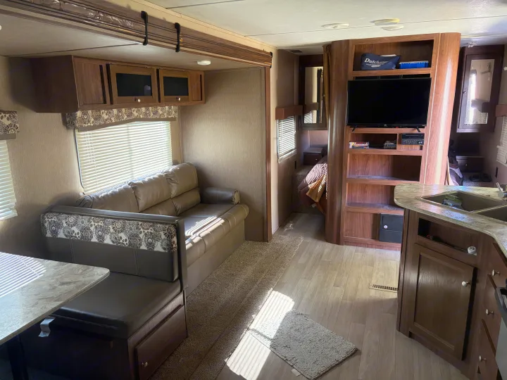 Explore this bright RV rental interior featuring a dinette, sofa, entertainment center, and kitchen, leading to a cozy bedroom.. Dutchmen Coleman Lantern 2018