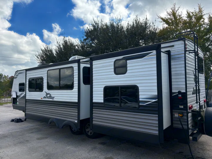 This RV rental, a white and gray travel trailer with an extended slide-out, is parked outdoors under a partly cloudy sky.. Jayco Jay Flight 2022