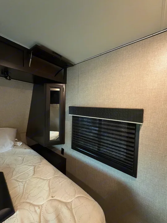 Experience comfort in this RV rental bedroom: featuring a quilted mattress, dark wood storage, and a privacy blind.. Jayco Jay Flight 2022