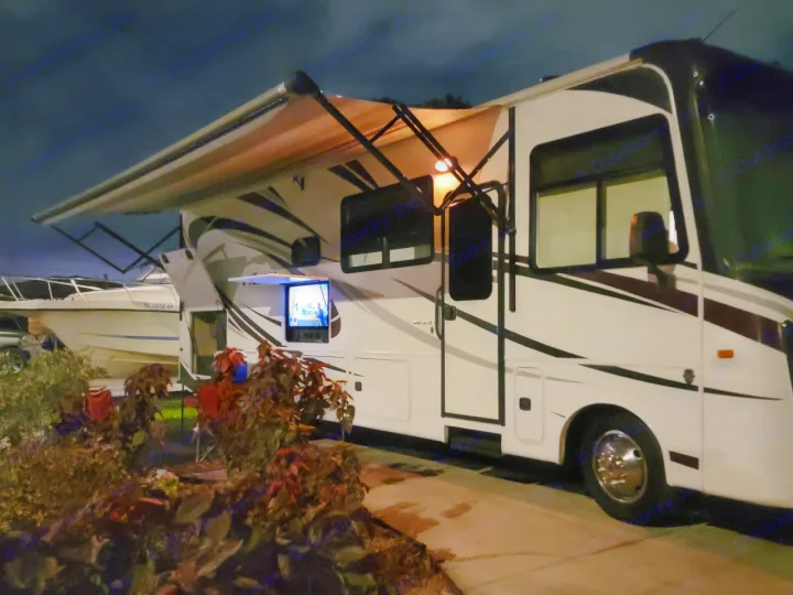 Nighttime RV rental setup with an extended awning, outdoor television, and a boat nearby.. Entegra Coach Vision 2019
