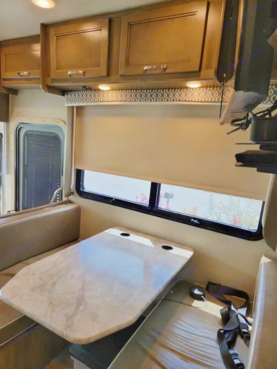 An inviting RV rental dinette with a dining table, padded bench seating, overhead cabinets, and a window view.. Entegra Coach Vision 2019