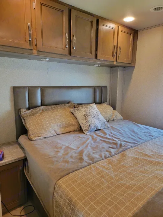 Cozy RV rental bedroom featuring an upholstered headboard, comfortable bed, and practical overhead storage cabinets.. Entegra Coach Vision 2019