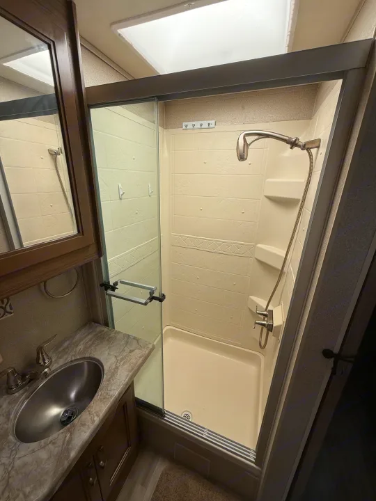 RV rental bathroom with a compact walk-in shower featuring sliding doors, a vanity with a sink, and a mirrored cabinet.. Entegra Coach Vision 2019