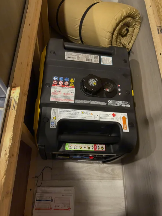 A portable generator and rolled-up sleeping bag are stored in a tight compartment, likely an RV rental. Warning labels visible.. Keystone RV Hideout Sport 2025
