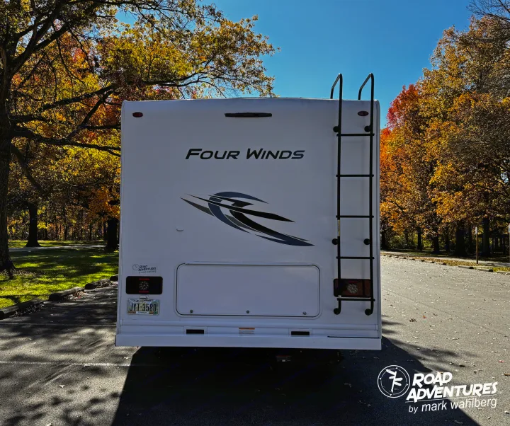 Rear of a white Four Winds RV rental with a ladder, parked among vibrant autumn trees, ready for a scenic road adventure.. Thor Motor Coach Four Winds 28Z 2024