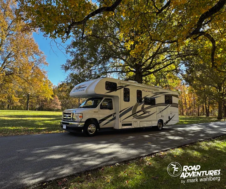 RV rental ready for autumn adventure! A white motorhome is parked on a road, surrounded by golden fall trees.. Thor Motor Coach Four Winds 28Z 2024