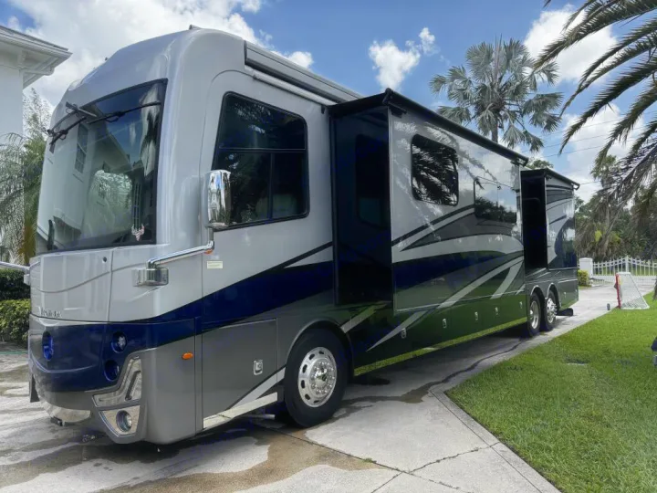 Sleek gray & blue motorhome rv rental, slide-outs extended, parked on a sunny driveway with palm trees.. Holiday Rambler Armada 2022