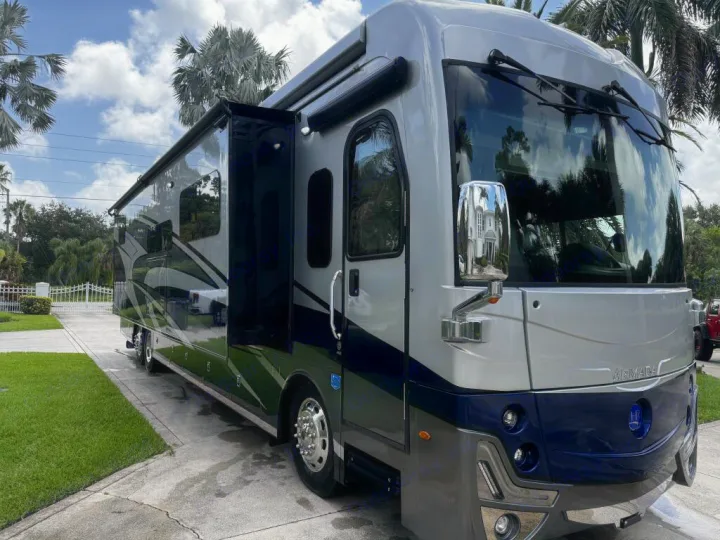 Experience comfort with this modern silver and blue luxury RV rental parked on a sunny driveway, surrounded by palm trees.. Holiday Rambler Armada 2022