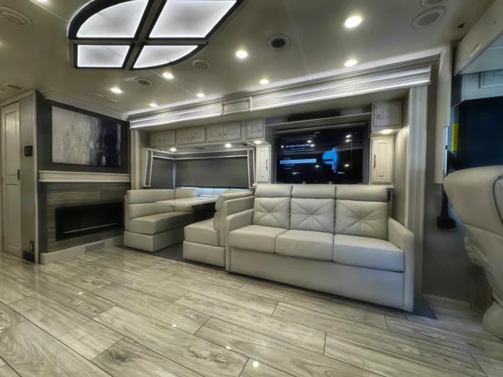 Spacious modern rv rental living area with a large sofa, dinette, TV, and fireplace. Features light wood flooring.. Holiday Rambler Armada 2022