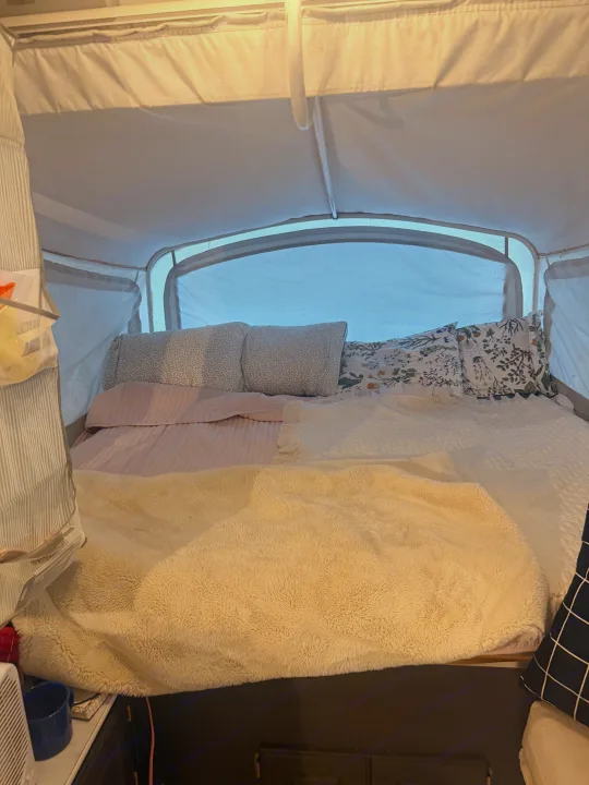 Inside a cozy rv rental, a pop-up camper bed features patterned pillows, soft pink sheets, and a fluffy beige blanket.. Coleman Grand Tour 2002