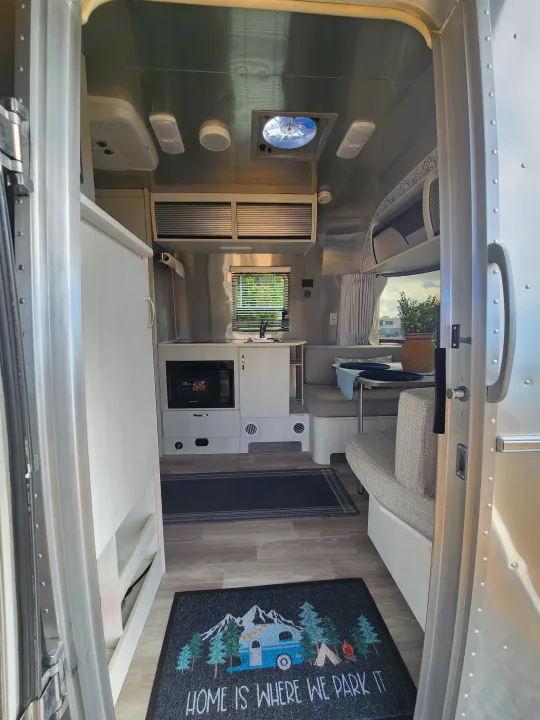 Cozy Airstream rv rental interior: compact kitchen, dining area, and entrance rug. Perfect for your next road trip adventure.. Airstream Bambi 2023