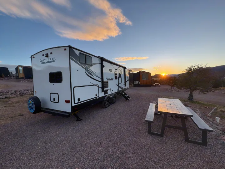 Enjoy a scenic RV rental experience! White travel trailer at a gravel campsite with a picnic table & sunset views.. Heartland RVs North Trail 2021