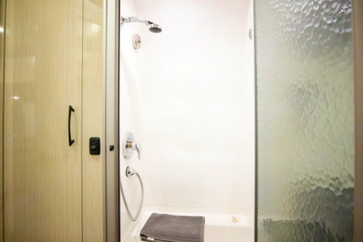 RV rental shower features a white stall, chrome fixtures, handheld sprayer, and a towel. Compact bathroom amenities.. Airstream International 2020