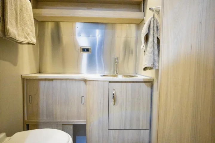Practical RV rental washroom showcasing a sink, light wood cabinets for storage, stainless steel backsplash, and toilet. Towels are ready.. Airstream Globetrotter 2019