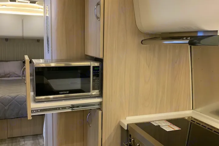 RV rental kitchen with a pull-out microwave and cooktop, offering convenient amenities for travel.. Airstream Globetrotter 2019