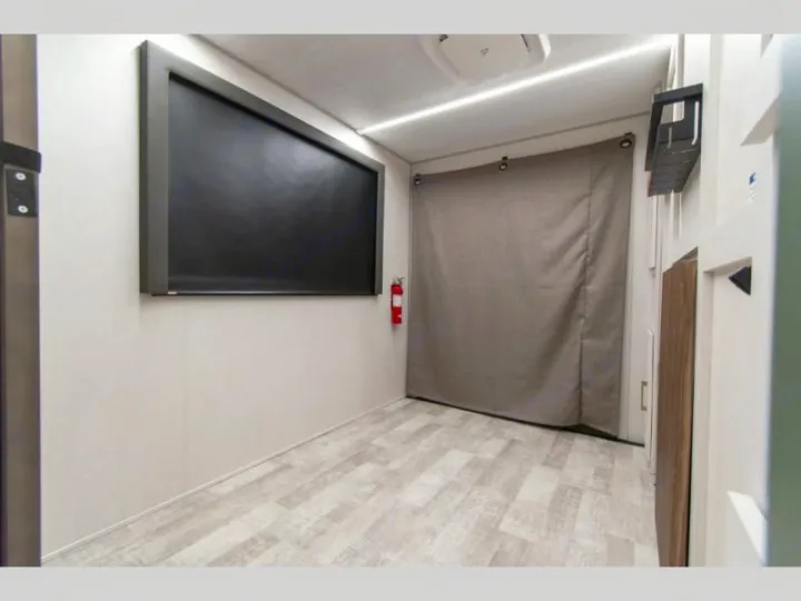 A compact modern RV rental interior showing a large wall-mounted screen, a fire extinguisher, and a curtained off area.. Forest River No Boundaries - RV Suite 1 2024