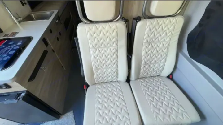 RV rental interior features cream quilted seats, a modern kitchen counter with a sink, and a digital control panel.. Winnebago Solis 2025