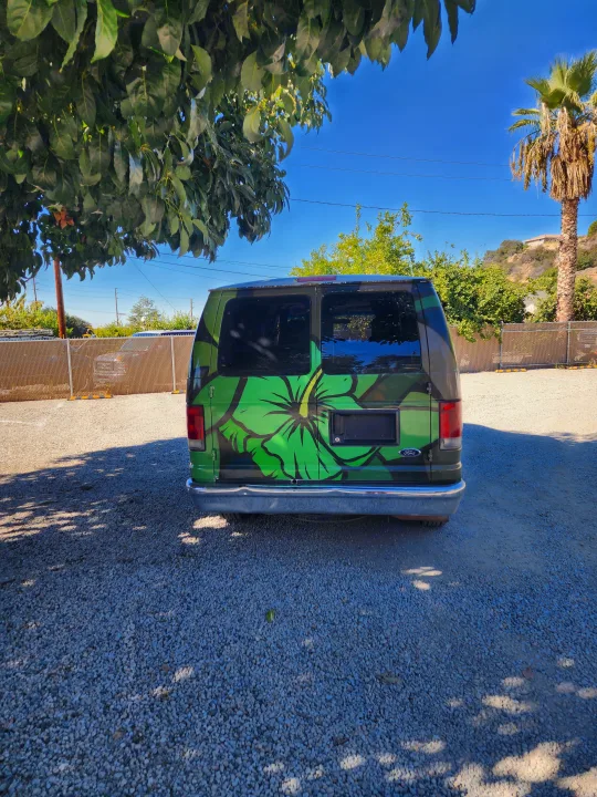 Rear of a custom green Ford van with a large hibiscus design, parked on a gravel lot. An ideal RV rental for a unique journey.. Escape Trailer Industries E150 XLT 2011