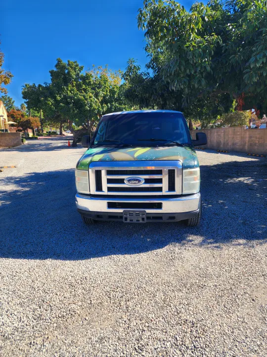 Front view of a green Ford van, excellent for RV rental, parked on gravel under a sunny blue sky.. Escape Trailer Industries E150 XLT 2011