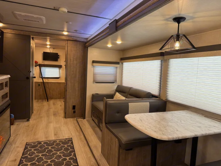 This cozy RV rental interior features a modern dinette with booth seating, a sofa, and wood-look flooring, offering comfort.. Forest River Surveyor 2023