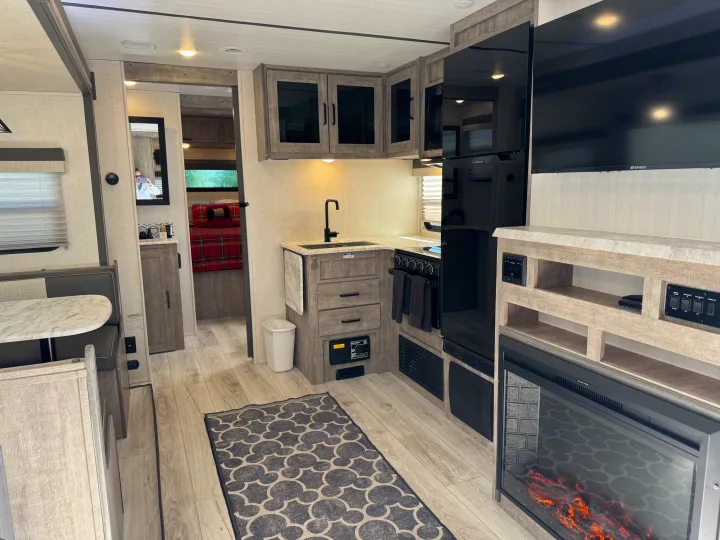 Spacious rv rental interior: kitchen, dining booth, fireplace, TV, and bedroom entrance for a cozy, modern experience.. Forest River Surveyor 2023