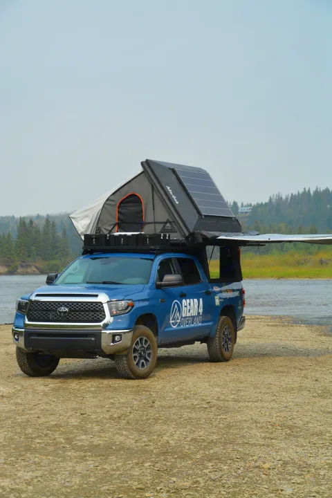 Blue overland truck with rooftop tent, solar, and awning by river, ready for RV rental-style adventures.. Toyota Tundra 2021