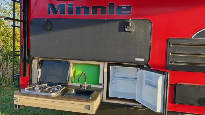 This RV rental's outdoor kitchen features a stove, sink, and open mini-fridge, perfect for camping adventures.. Minnie Minnie Trailer 2019
