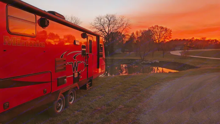 Experience the magic of an RV rental with this Minnie travel trailer glowing under a vibrant red sunset, reflecting in a peaceful pond.. Minnie Minnie Trailer 2019