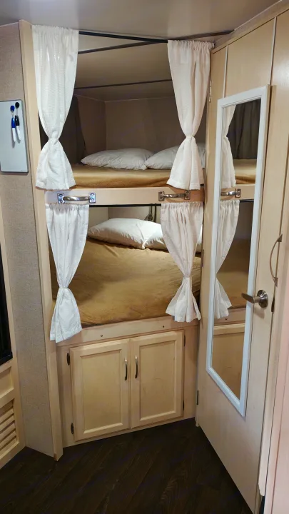 RV rental interior shows cozy bunk beds with privacy curtains, light bedding, and built-in cabinets below, plus a door mirror.. Minnie Minnie Trailer 2019
