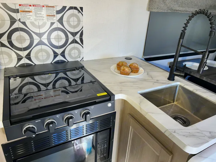 This modern **RV rental** kitchen features a compact stove, oven, sink, stylish backsplash, and fresh muffins on the countertop.. Forester LE 2026
