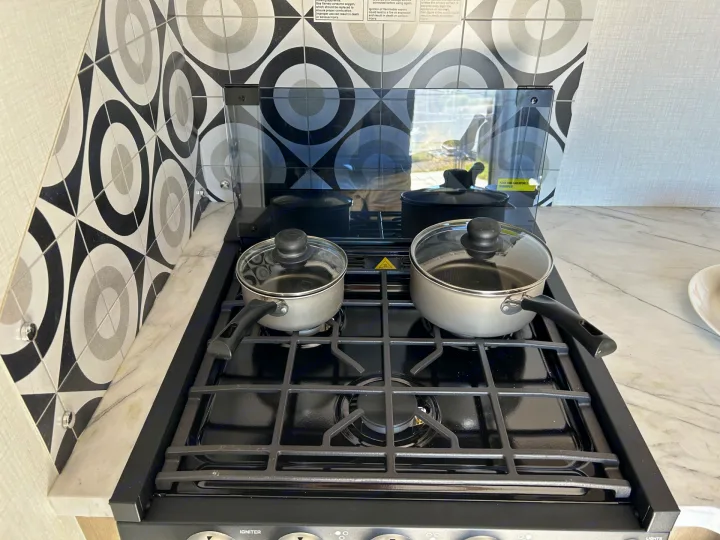 Cooking setup in an rv rental: a gas stovetop with two pots, a raised glass cover, and a geometric tile backsplash.. Forester LE 2026