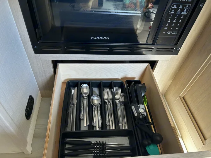 Inside an RV rental kitchen: an open drawer neatly displays cutlery and cooking tools below a Furrion microwave.. Forester LE 2026