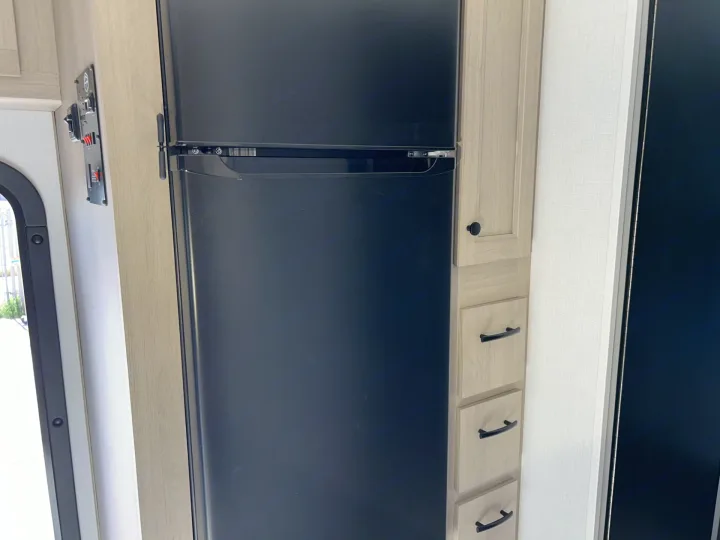 This RV rental features a black two-door refrigerator, light wood cabinets with drawers, and an interior control panel.. Forester LE 2026