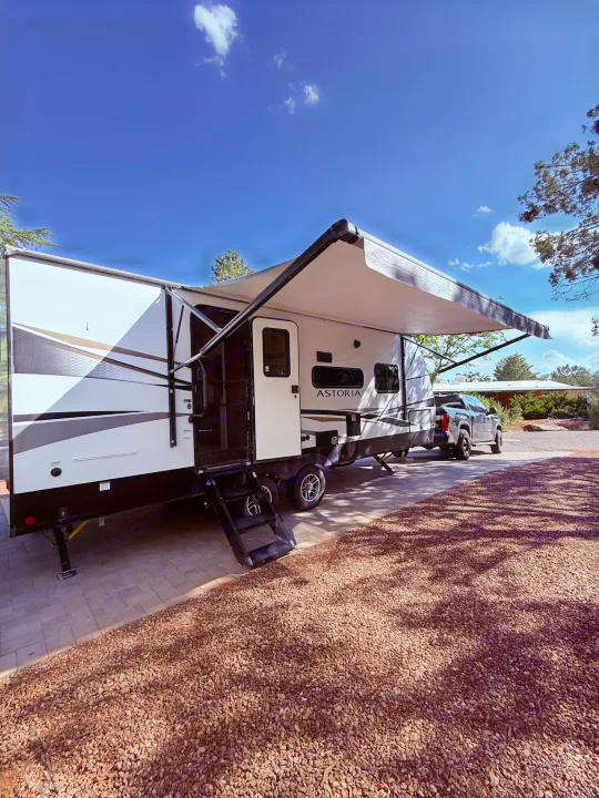 A modern RV rental with an extended awning, parked on pavers with a truck in tow, ready for your camping trip.. Astoria Astoria Trailer 2022