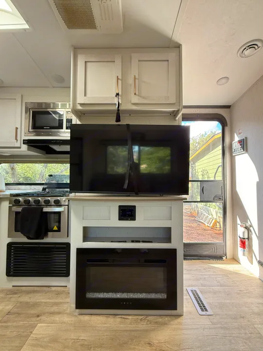 Bright RV rental interior showcasing a modern kitchen with stove, microwave, and a cozy living area with TV and fireplace.. Astoria Astoria Trailer 2022