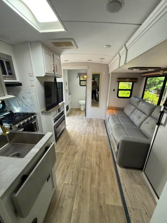 Modern rv rental interior: kitchen, living area with grey sofa, and bathroom. Bright and ready for adventure!. Astoria Astoria Trailer 2022