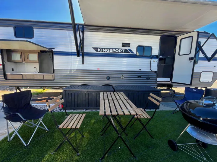 RV rental setup with outdoor kitchen, awning, and patio furniture on green turf, ready for outdoor living.. Gulf Stream Kingsport 2023