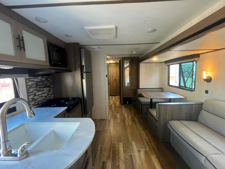 Bright rv rental interior featuring a modern kitchen, booth dinette, and cozy sofa with wood-look floors.. Gulf Stream Kingsport 2023