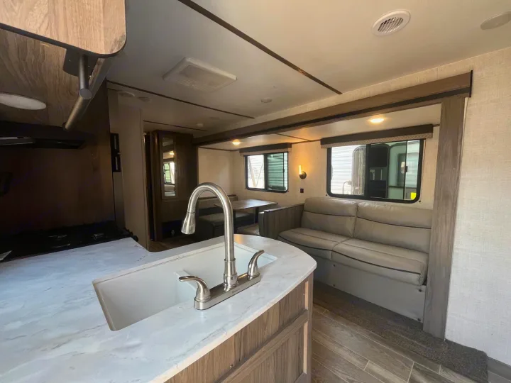 Bright RV rental interior, featuring a well-equipped kitchen with sink, inviting sofa, and dining area for comfortable travel.. Gulf Stream Kingsport 2023