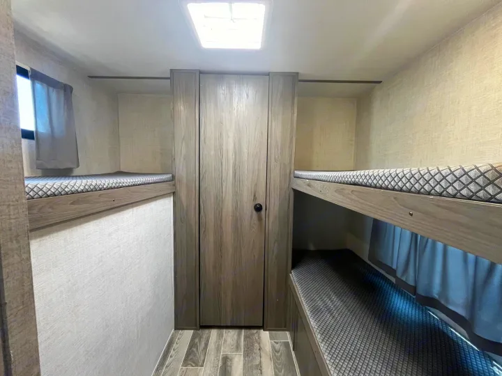 This RV rental bunkhouse features cozy sleeping areas with diamond-patterned mattresses, a central wardrobe, and a window.. Gulf Stream Kingsport 2023