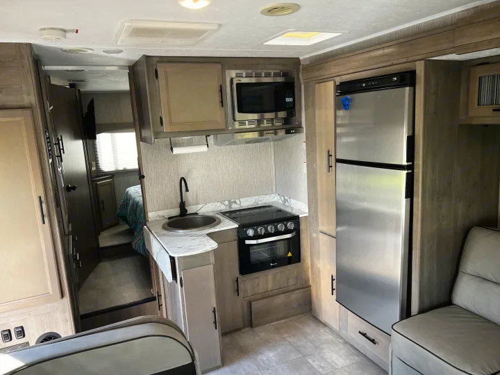 This rv rental offers a modern kitchen setup with a stainless steel fridge, microwave, stove, and sink. Light wood accents.. Forest River Coachmen Freelander Premier 2021