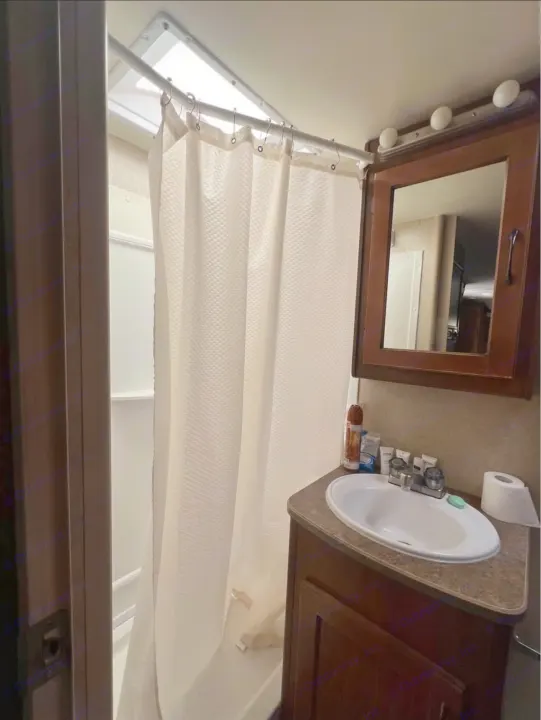 Compact RV rental bathroom with shower, sink vanity, mirror, and toiletries.. Lance Manufacturing Lance Manufacturing Trailer 2016